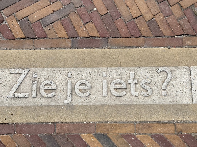 Foto eines Schriftzugs auf dem Bürgersteig: ZIe je iets? Auf Niederländisch: Siehst du etwas?
